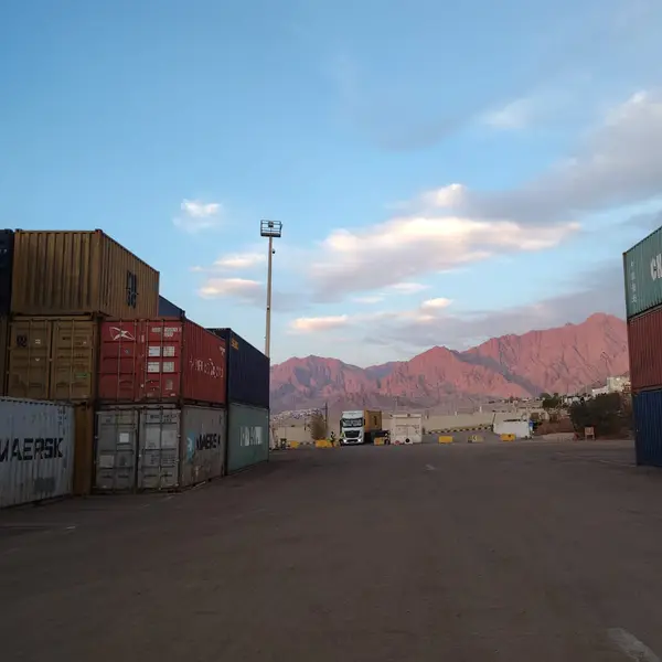 Aisle between container stacks at the Aqaba yard, with the mountains behind